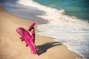 Woman in airy crimson dress dancing on the beach